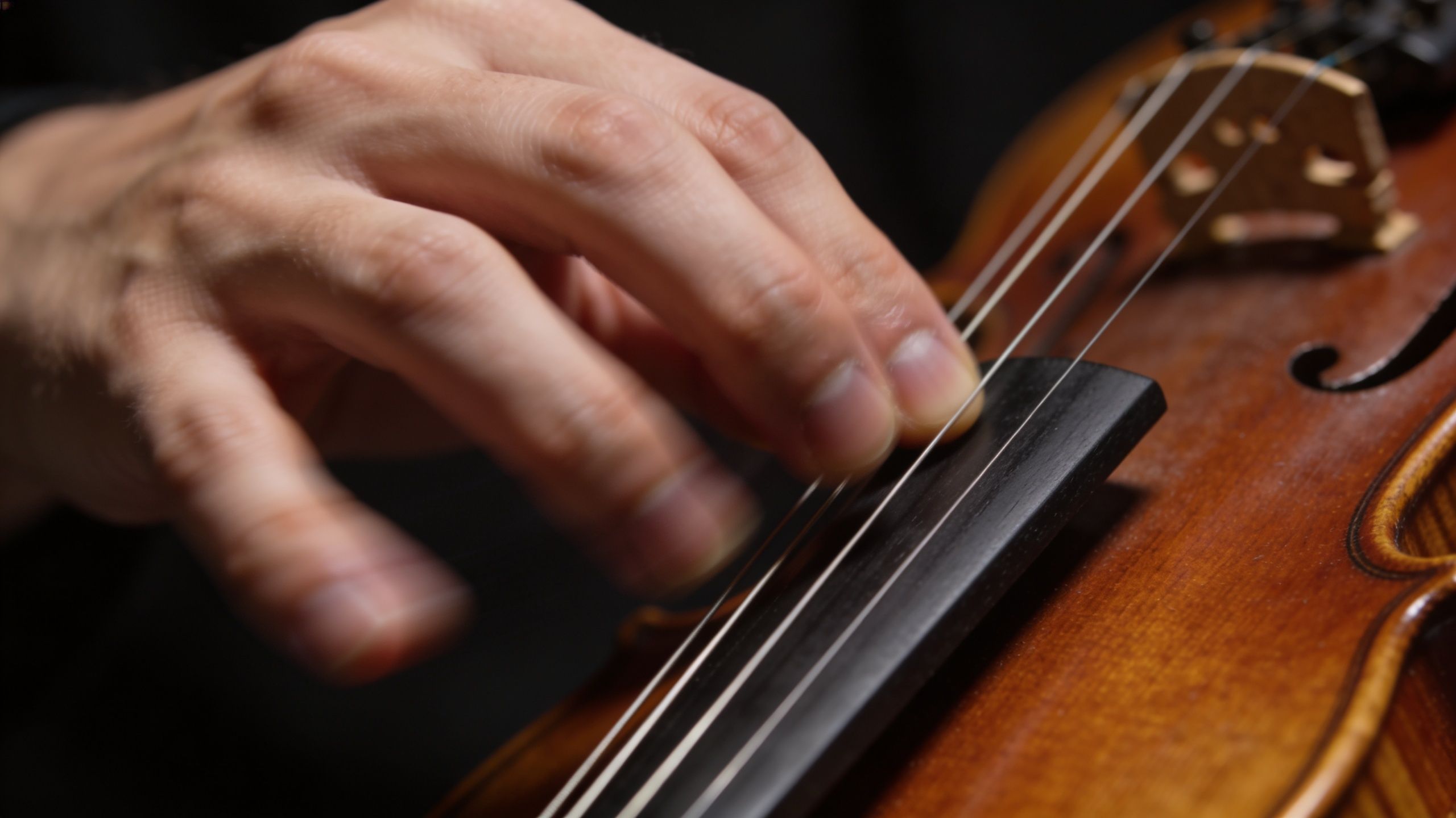 A close up view of a musician's hand playing notes on a wooden violin fingerboard.